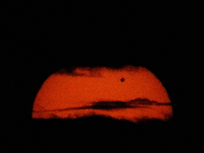 Black sky and clouds with a deep red Sun. Venus is a black dot in front of the Sun